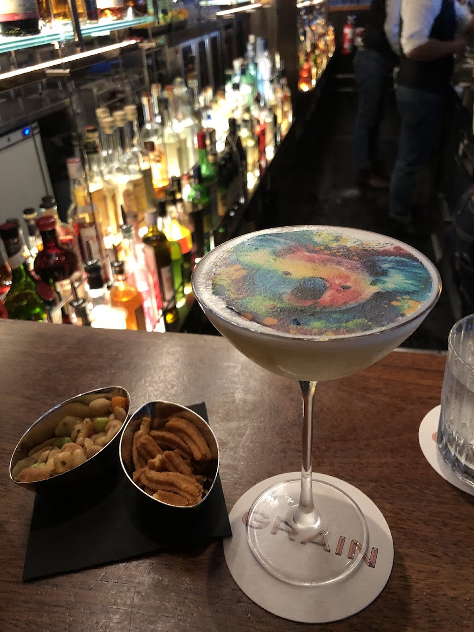 Cocktail served at the Grain Bar counter with snacks nearby